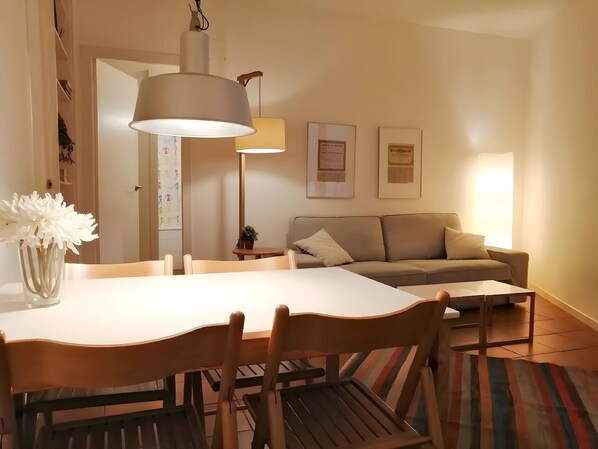 A dining area with a table, chairs, a hanging lamp, a sofa, and framed certificates on the wall.