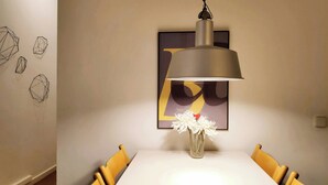 Un espace repas comprenant une table, des chaises, un luminaire suspendu et une œuvre d’art encadrée accrochée au mur.