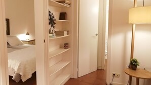 Une chambre à coucher comprenant un lit, une table de chevet, une lampe et une armoire blanche avec des étagères.