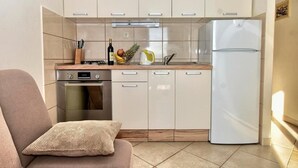 Een compacte keuken met een inbouwoven, een witte koelkast en een aanrecht met een fruitschaal en een waterkoker.