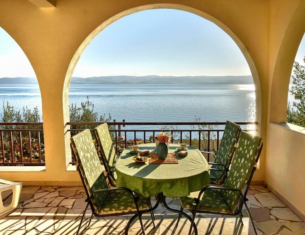 A round table with chairs on a balcony overlooking a body of water.