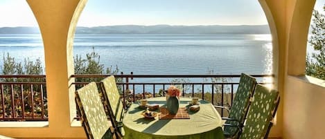 A round table with chairs on a balcony overlooking a body of water.