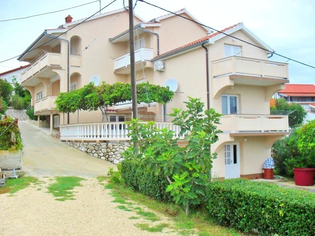 A multi-story residential building with balconies, a stone staircase, and a gravel driveway.