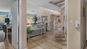 Amplia sala de estar con piso de madera, una escalera y una cocina al fondo.
