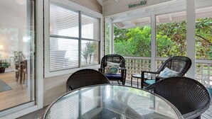 Un patio cubierto con mobiliario de mimbre, una mesa de vidrio y vistas a la vegetación.