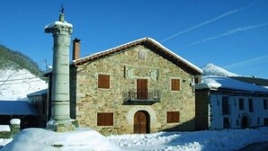 Un edifici de pedra amb una entrada central i persianes de fusta, envoltat de neu.