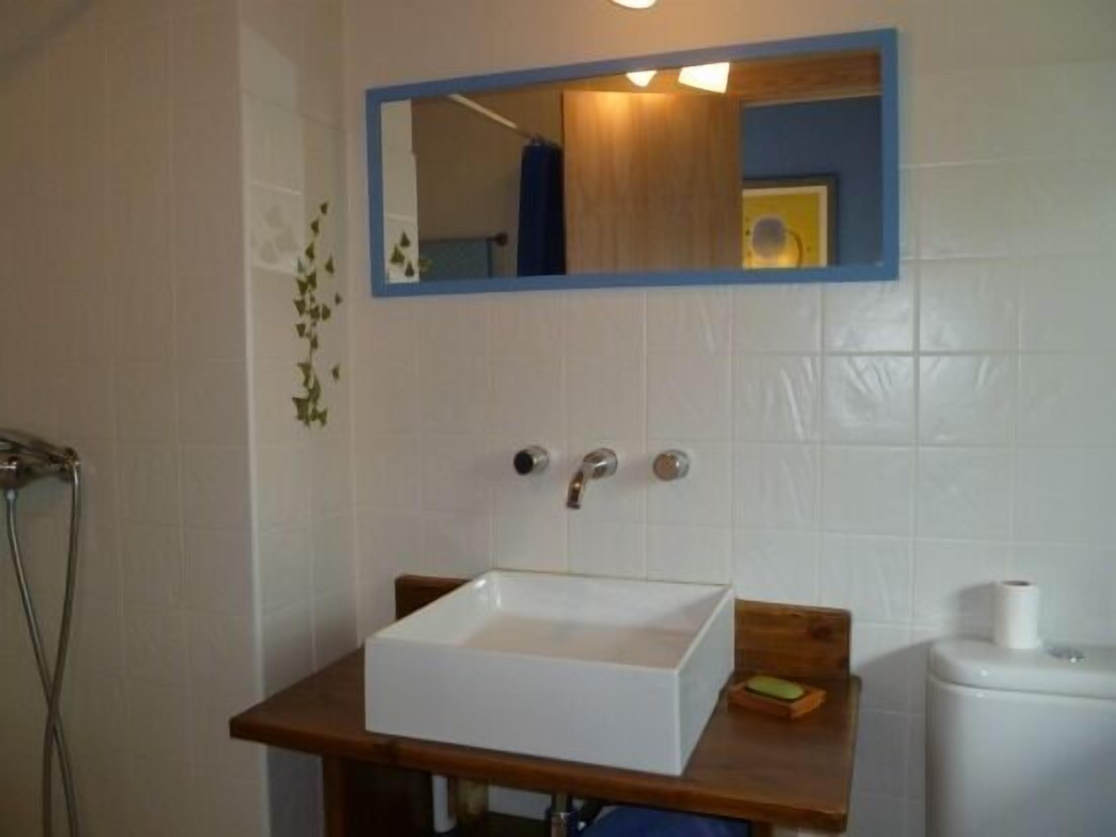 Une salle de bain avec un lavabo blanc, un plan de toilette en bois et un miroir au-dessus.