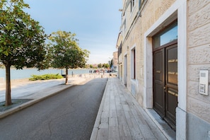 A coastal street with a sidewalk, trees, and a building with a door and a security keypad. - Deluxe Apartment Nina by the sea in Porec, Istria (Porec)