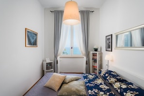 Une chambre à coucher avec un lit, une fenêtre avec des rideaux, une table de chevet, une lampe et une bibliothèque.