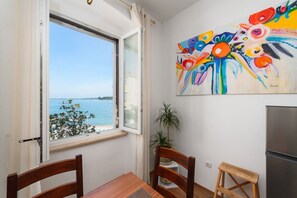 Une pièce comprenant une table à manger, des chaises, une fenêtre donnant sur la mer et une peinture abstraite aux couleurs vives accrochée au mur.