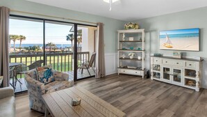 A spacious living room with a large sliding glass door leading to a balcony, a ceiling fan, a television mounted on the wall, and a wooden coffee table. - 2 Bedroom Townhome with a Gulf View and King Beds (Miramar Beach)