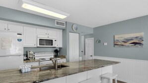 A modern kitchen with white cabinetry, a marble countertop, a stainless steel sink, and a microwave. There are two white bar stools and a clock on the wall. - 2 Bedroom Townhome with a Gulf View and King Beds (Miramar Beach)