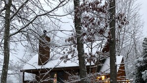 Uma cabana de madeira com vários níveis, rodeada por árvores cobertas de neve e pelo chão coberto de neve.