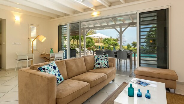 Un salon moderne avec un canapé beige, une table basse blanche et une porte vitrée donnant sur un patio extérieur avec une piscine.