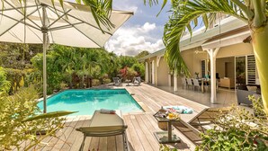 Une terrasse en bois avec une piscine, des chaises longues et des parasols.
