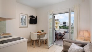 Ett kompakt bostadsutrymme med ett litet kök, en matplats och en balkong med utsikt över byggnaderna.