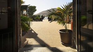 Una puerta que da a un patio con plantas en macetas, un banco de piedra y vistas de una montaña.