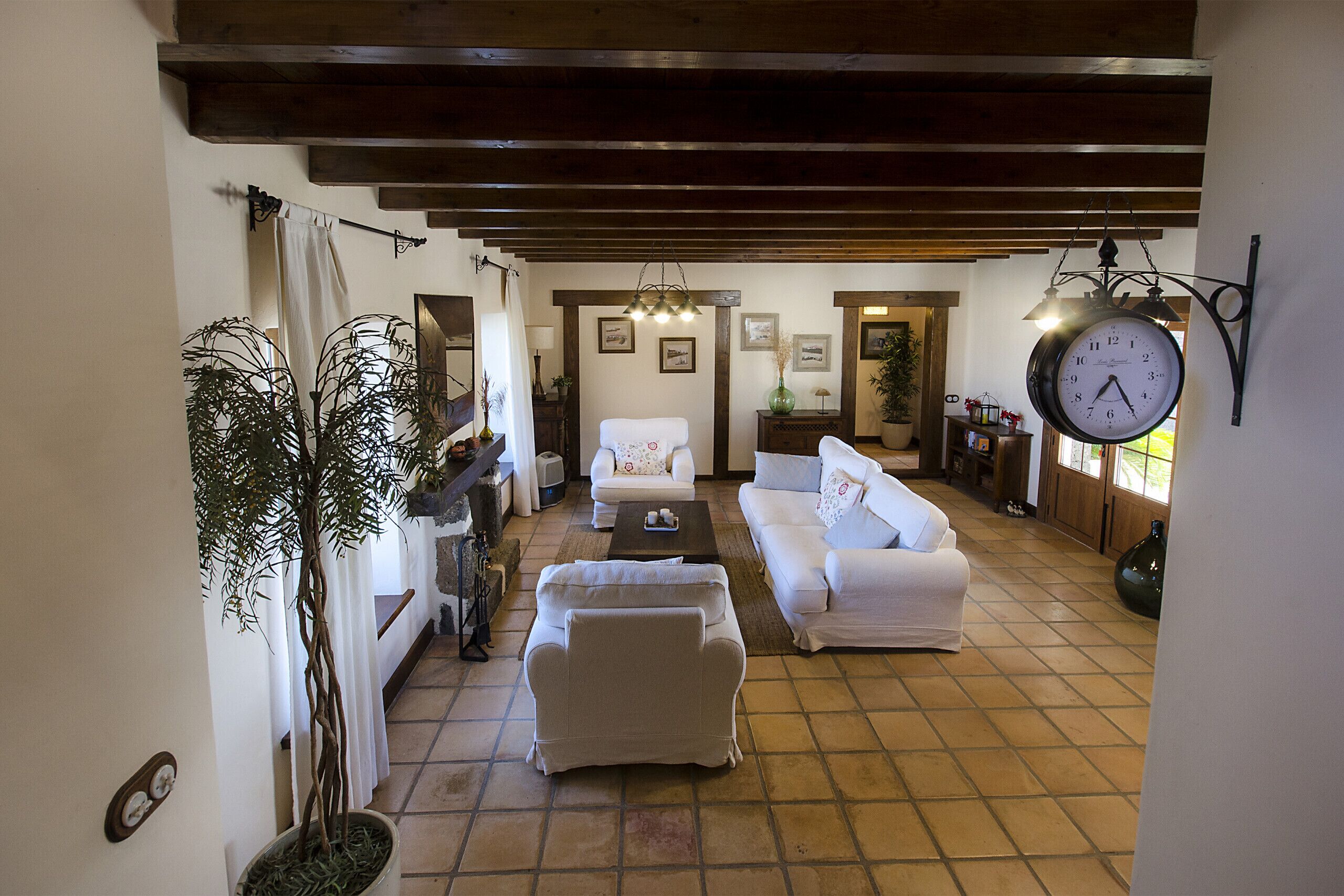 A spacious living room with a large clock, white sofas, and a potted plant.