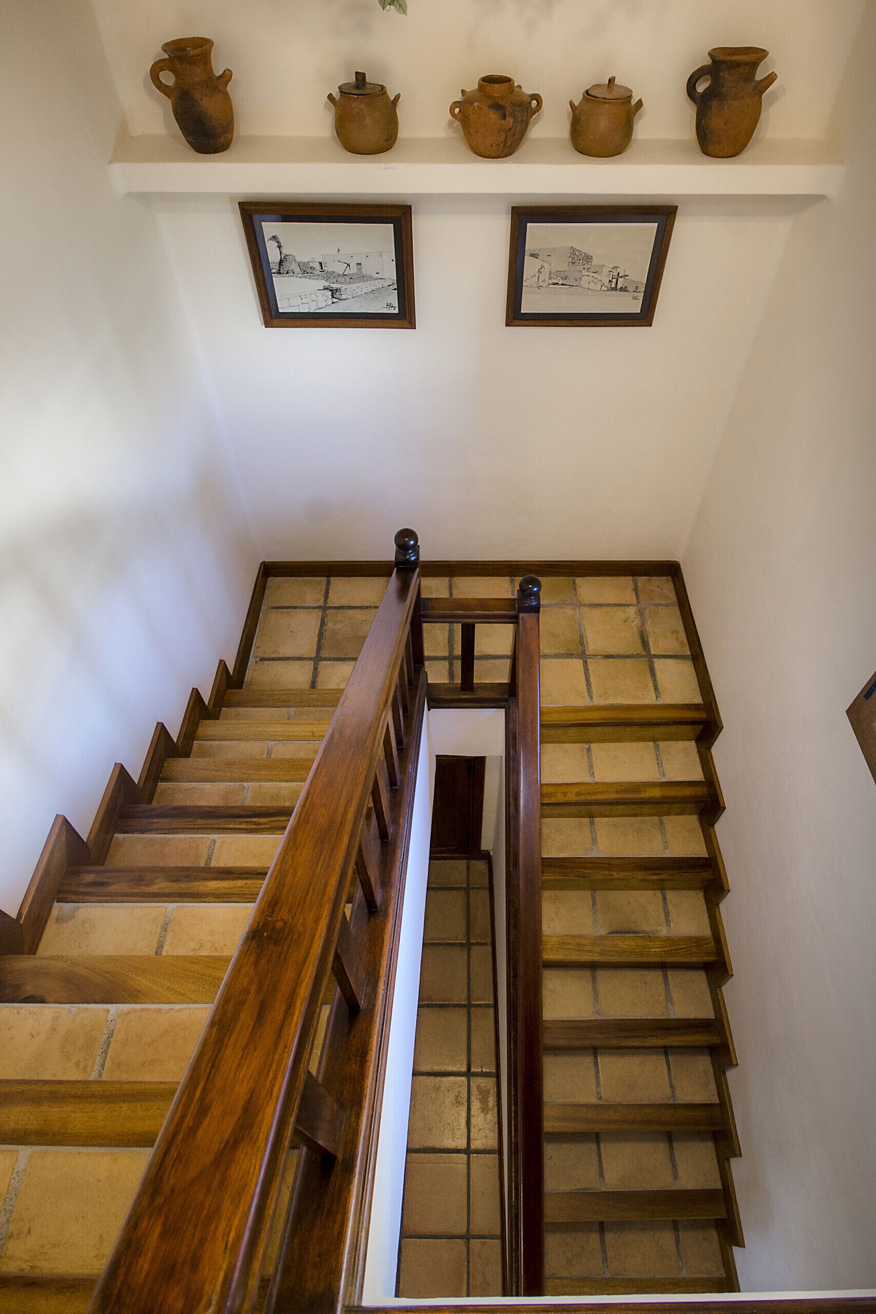 A wooden staircase with a handrail, leading to a landing with a shelf holding pottery and framed artwork.