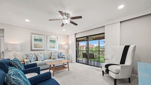 A living room with a sofa, armchairs, a coffee table, a ceiling fan, and a balcony with a view. - Partial Beach View 2 bed, 2 bath at Sanibel Moorings #732 (Sanibel)