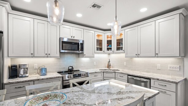 A kitchen with white cabinetry, a microwave, a stove, a sink, and a bowl on the counter. - Partial Beach View 2 bed, 2 bath at Sanibel Moorings #732 (Sanibel)