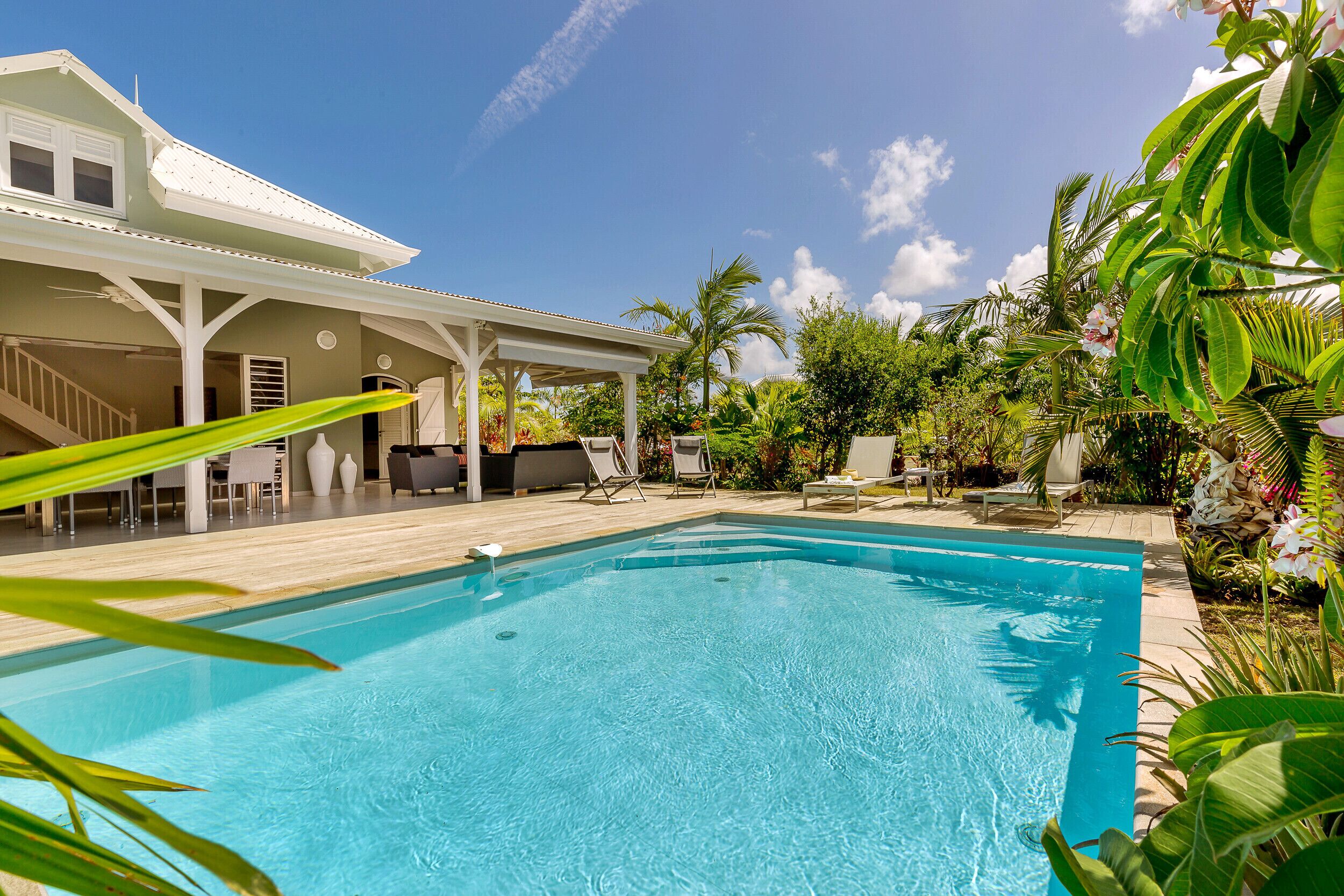 A swimming pool with a covered patio area, lounge chairs, and a staircase leading to the house.