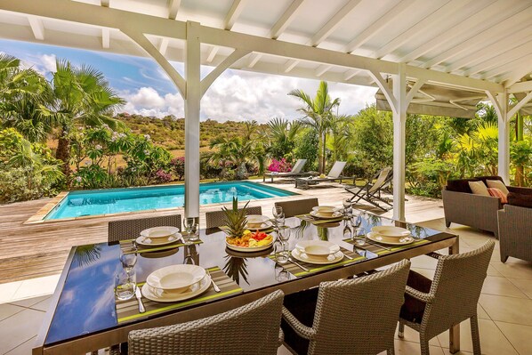 Enjoy a formal dining experience under a shaded pergola with a pool view.