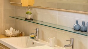 Un baño moderno con un lavabo grande blanco, dos grifos cromados y un estante de vidrio sobre el lavabo.