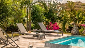 Zona de piscina con sillones, una mesa y la piscina.