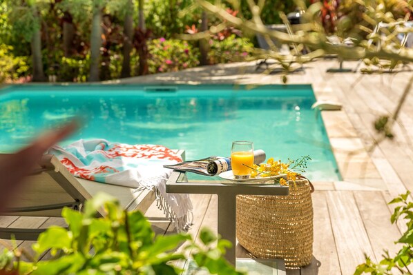 A poolside area with a lounge chair, a table with a drink, and a wicker basket.