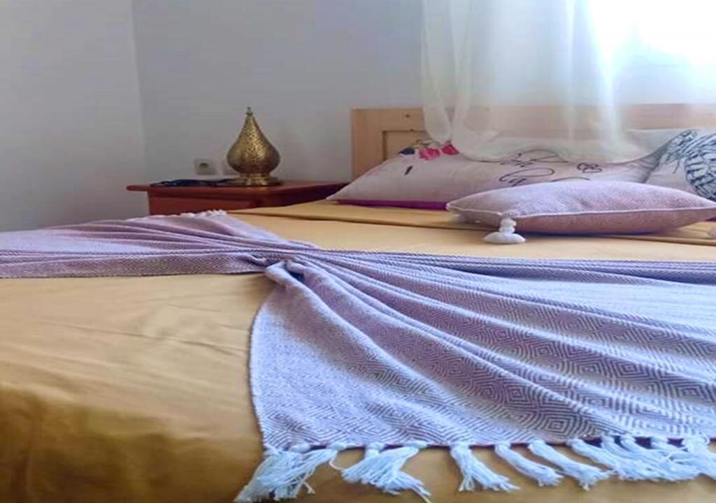 A bed with a patterned blanket and a decorative lamp on a bedside table.