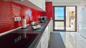 A modern kitchen with a red backsplash, a black countertop, and a view of the laundry area through an open door.