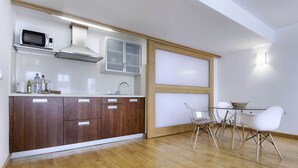 Una cocina moderna con armarios de madera, microondas y un comedor con mesa de vidrio y sillas blancas.