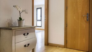 Un pasillo con piso de madera, un tocador blanco con dos cajones y una puerta de madera.