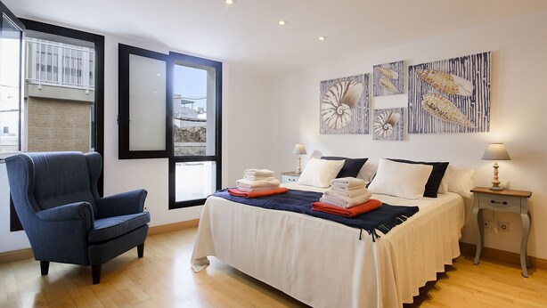 Un dormitorio con una cama, una silla, una mesita de noche y una obra de arte en la pared.