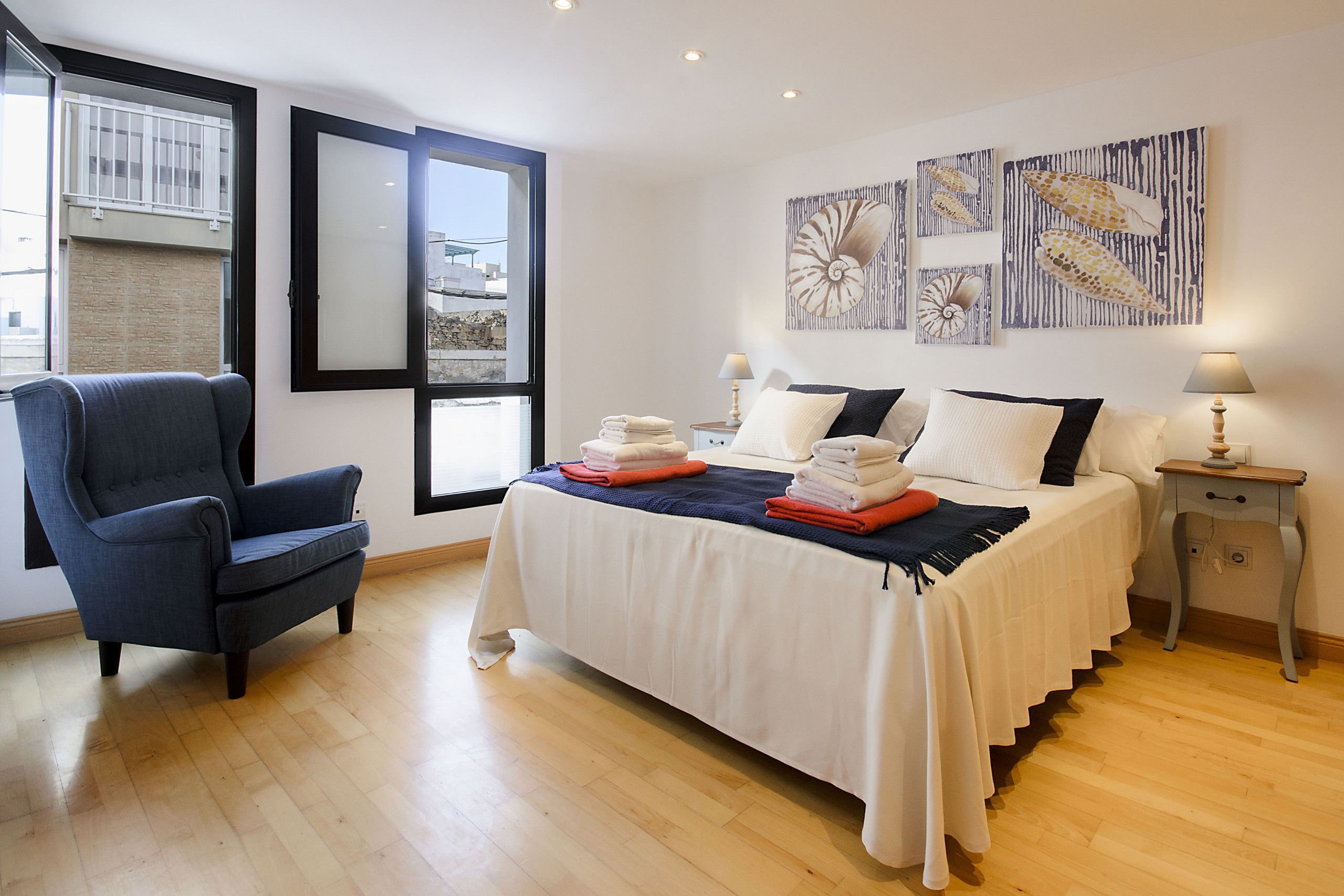 A bedroom with a bed, a chair, a nightstand, and artwork on the wall.