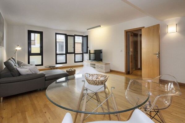 A modern living room with a glass table, a grey sofa, and a TV.