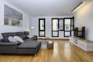 A modern living room with a grey sectional sofa, a TV on a wooden stand, and a large window with black frames. - El Estudio de Lela, Your very home in the heart of Arrecife (Arrecife)