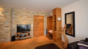 A modern living room with a stone wall, wooden door, built-in TV stand, and a large mirror. - Zell City Exclusive Lodges - TOP 4 (Zell am See)