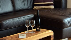 A wooden table with a bottle of wine and two glasses on it, placed in front of a black leather sofa. - Zell City Exclusive Lodges - TOP 4 (Zell am See)