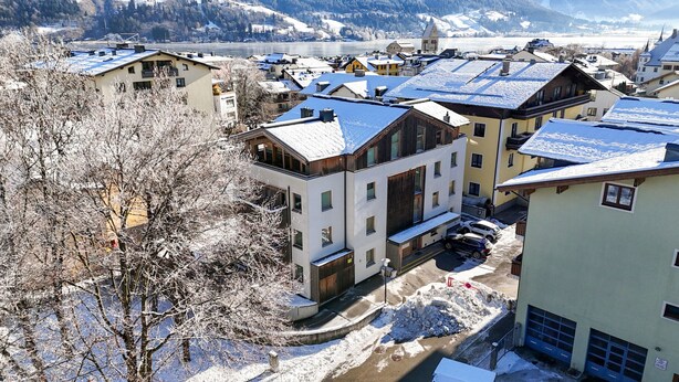 A snow-covered residential area with modern buildings, a visible church, and a river in the background. - Zell City Exclusive Lodges - TOP 4 (Zell am See)