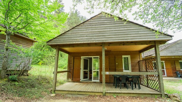 Een houten hut met een veranda, een tafel en stoelen.