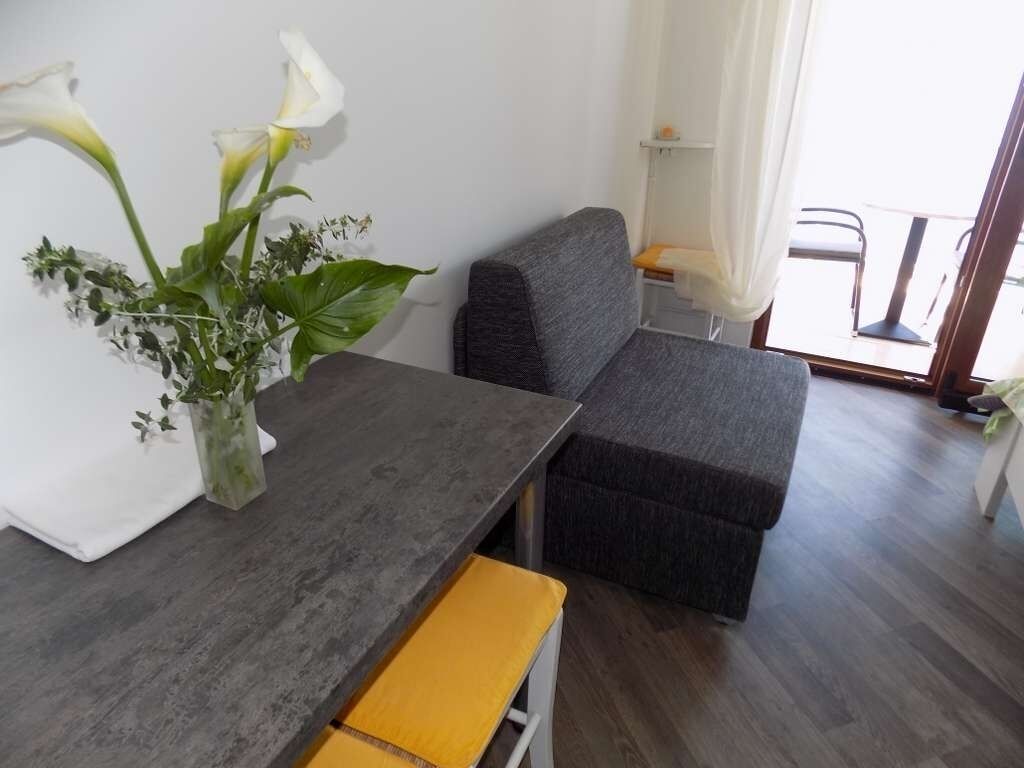 A modern room with a grey sofa, a small table with a yellow cushion, and a vase with white flowers.