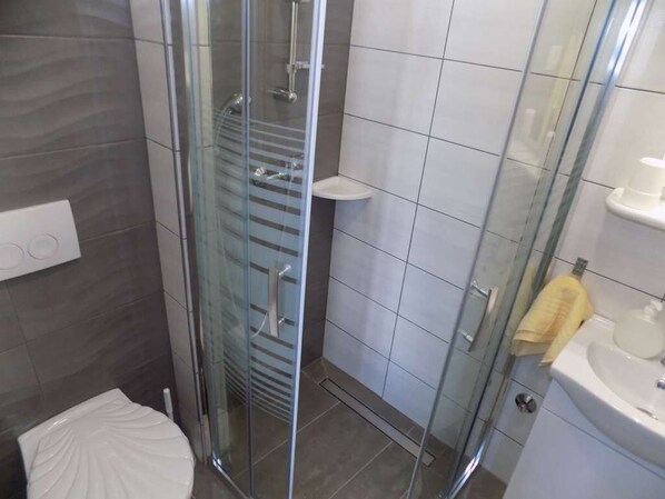 A modern bathroom with a glass shower enclosure, a white toilet, and a sink with a yellow towel.