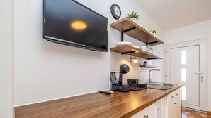 Eine moderne Küche mit Flachbildfernseher, Holzarbeitsplatte, eingebauten Regalen und einer Kaffeemaschine.
