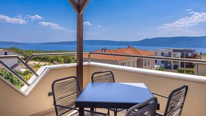 Ein Balkon mit Tisch und Stühlen, der Blick auf die Küste mit Gebäuden und einem klaren Himmel gewährt.