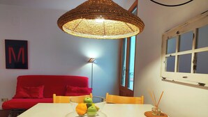 Zona de dinar amb taula, cadires, un plat de fruita, llum penjant, sofà vermell i finestra amb vistes.