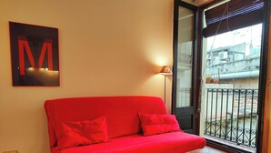 Un sofà vermell amb rodes a una habitació amb terra de rajola, una làmpada penjada a la paret i un gran cartell amb la lletra 'M'.