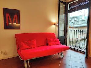 A red sofa with wheels in a room with a tiled floor, a wall-mounted lamp, and a large letter 'M' sign.