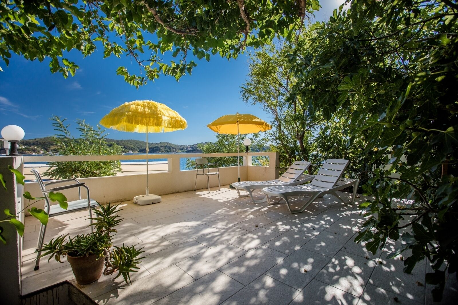 Eine Dachterrasse mit zwei gelben Sonnenschirmen, Liegestühlen und Topfpflanzen.